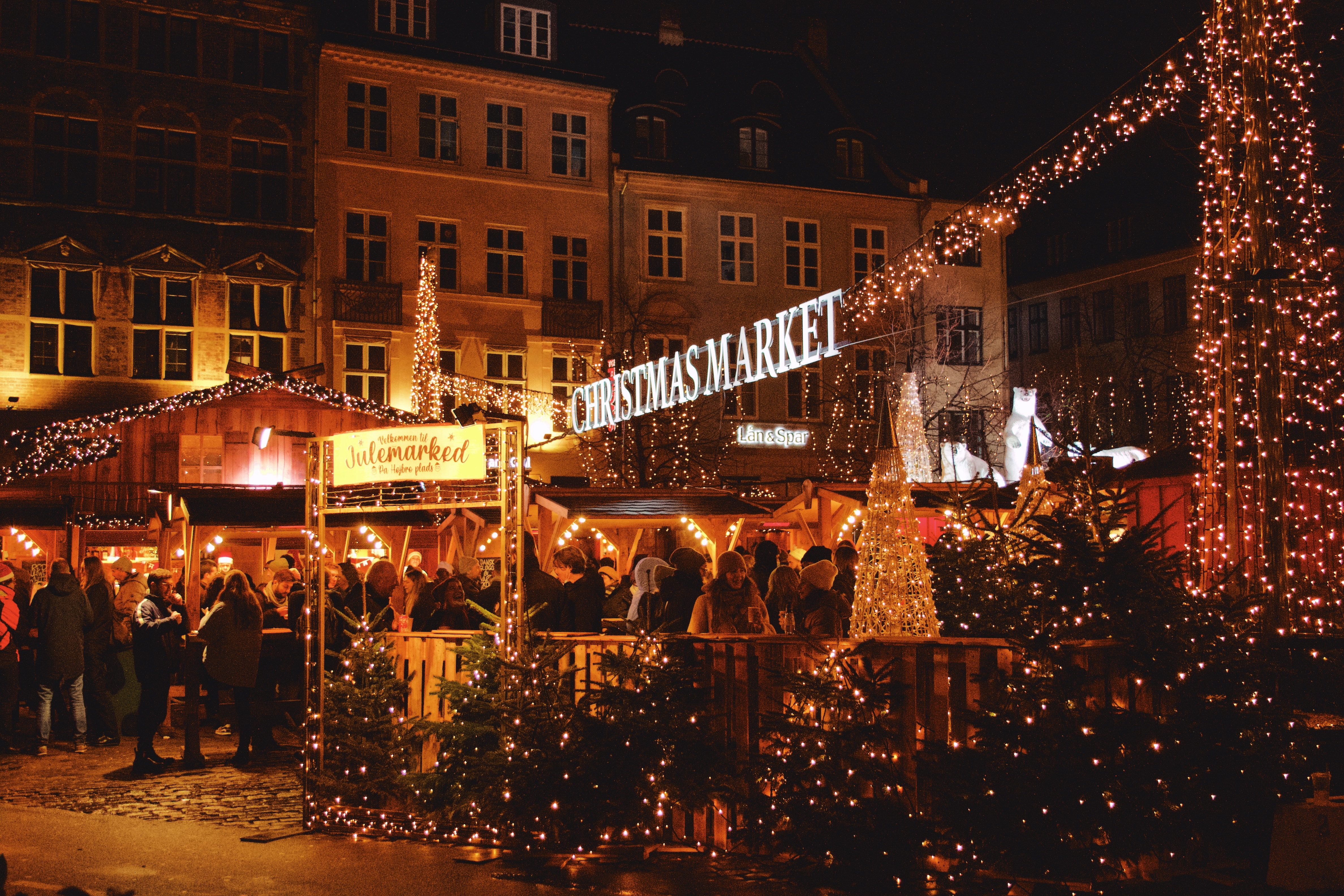 Bustling Christmas market in Copenhagen with illuminated stalls, sparkling lights, and visitors enjoying the festive atmosphere.