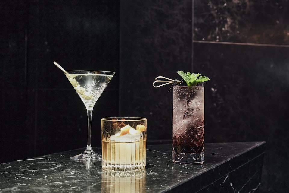 Elegant cocktails displayed on a marble counter with a luxurious dark tiled background in a hotel setting.