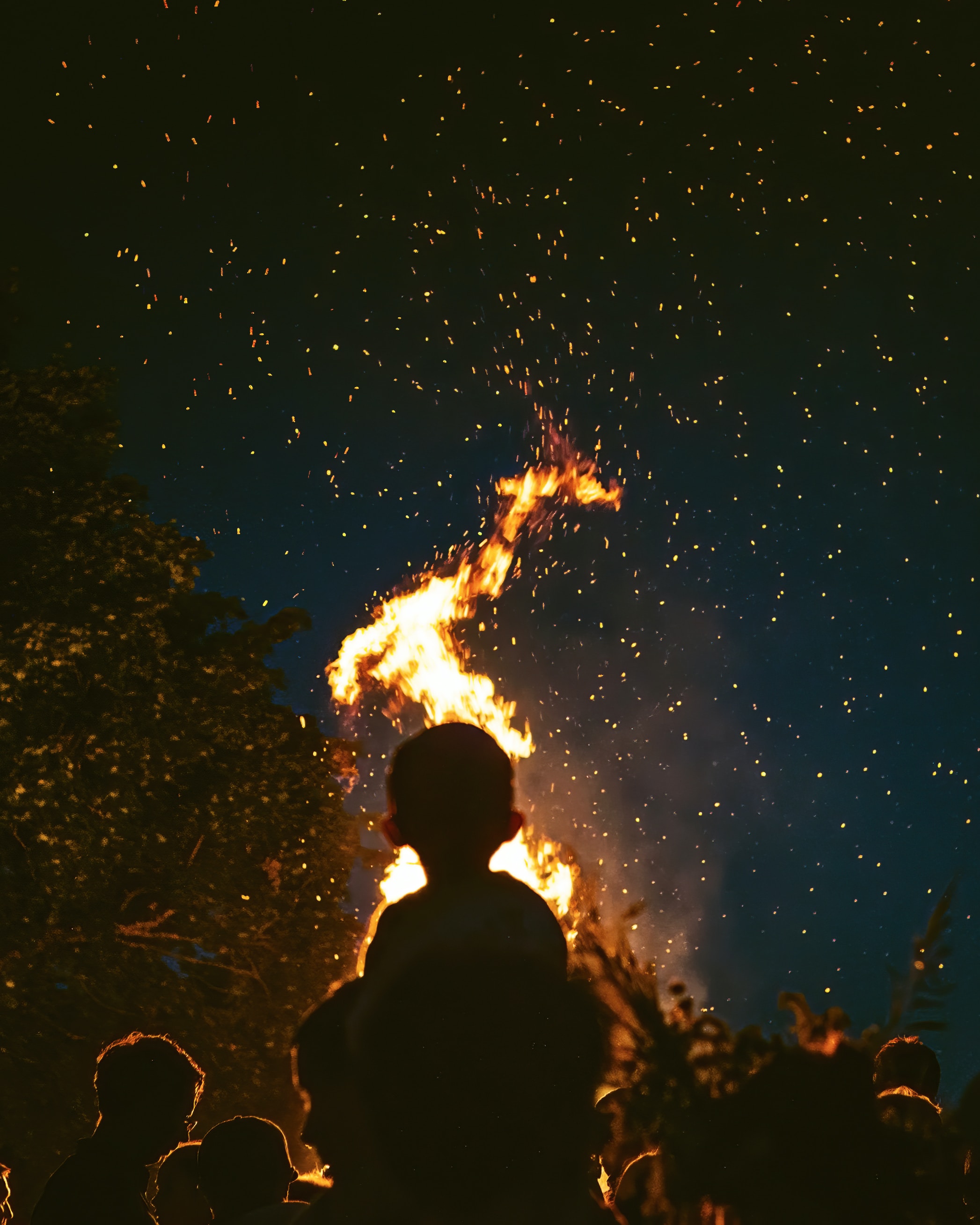 Silhouette of a person observing a vibrant Midsummer Night's bonfire with sparks flying against a dark sky in Copenhagen.