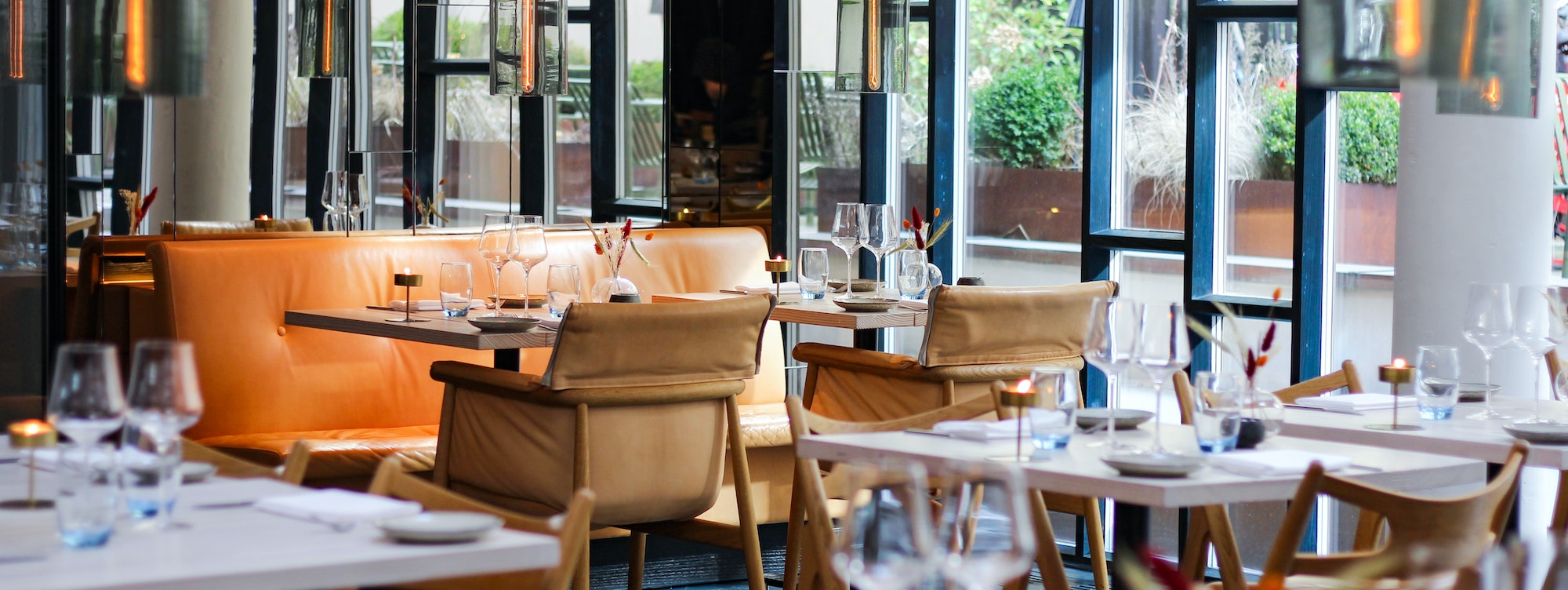 Elegant hotel dining area with leather seating, ambient lighting, and set tables by large windows.