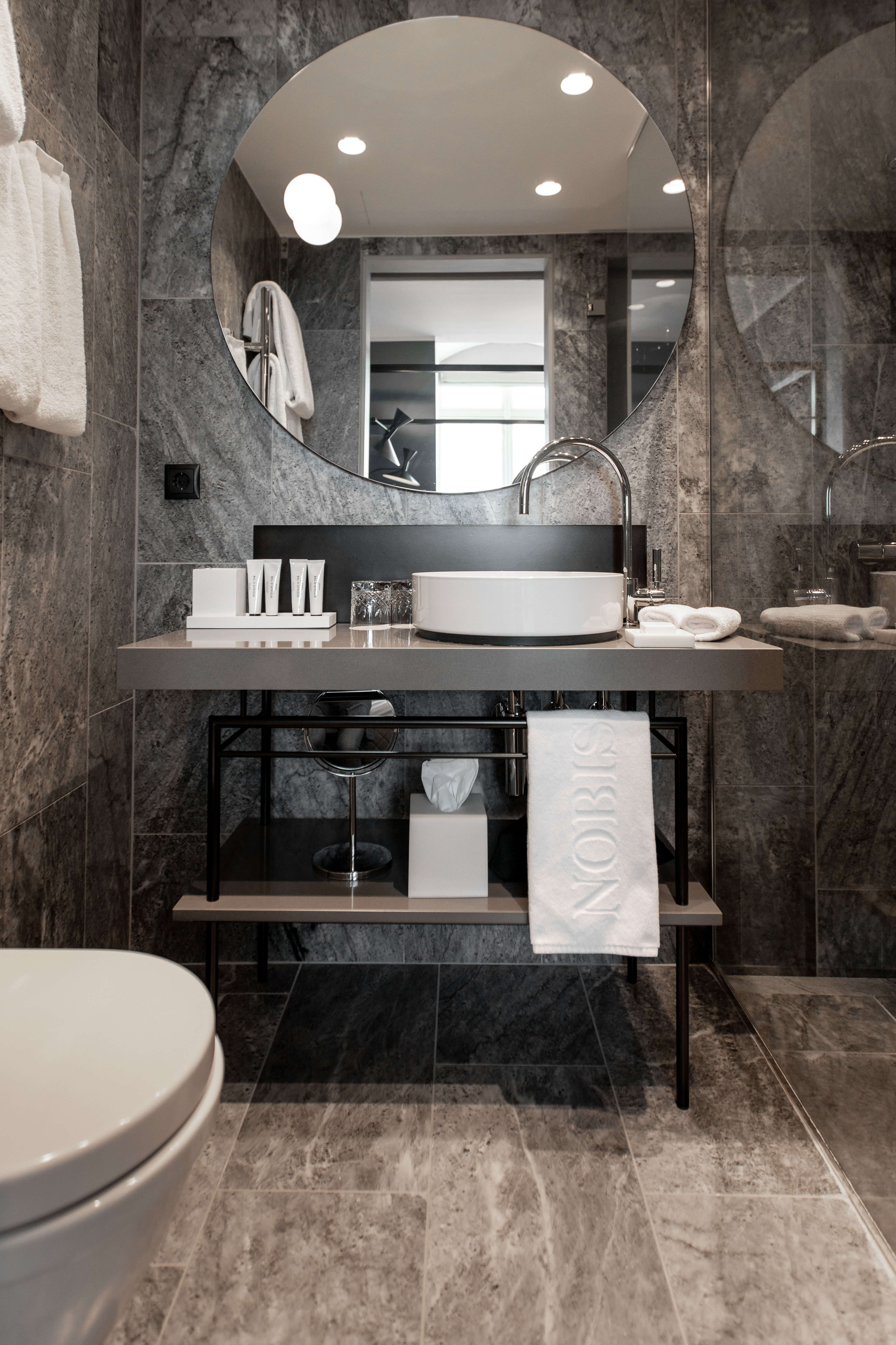 Modern hotel bathroom interior with marble tiles, elegant vanity, and branded 'NOBIS' towels.