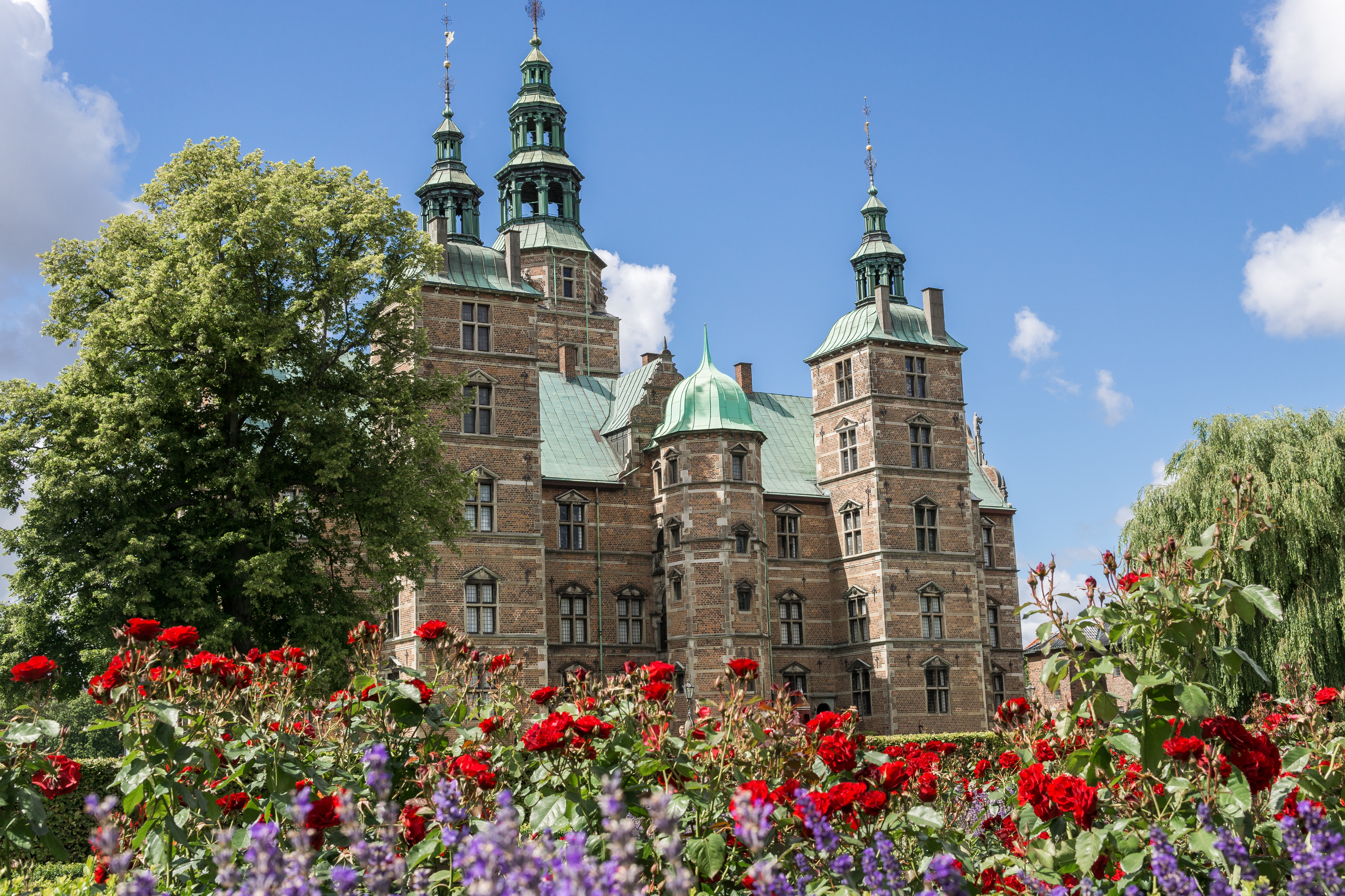 Rosenborg Castle in Copenhagen, Denmark, surrounded by vibrant red and purple flowers under a clear blue sky, showcasing its Renaissance architecture.