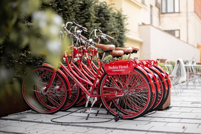 Row of red bicycles branded with 'Nobis Hotel Copenhagen' parked in a courtyard.