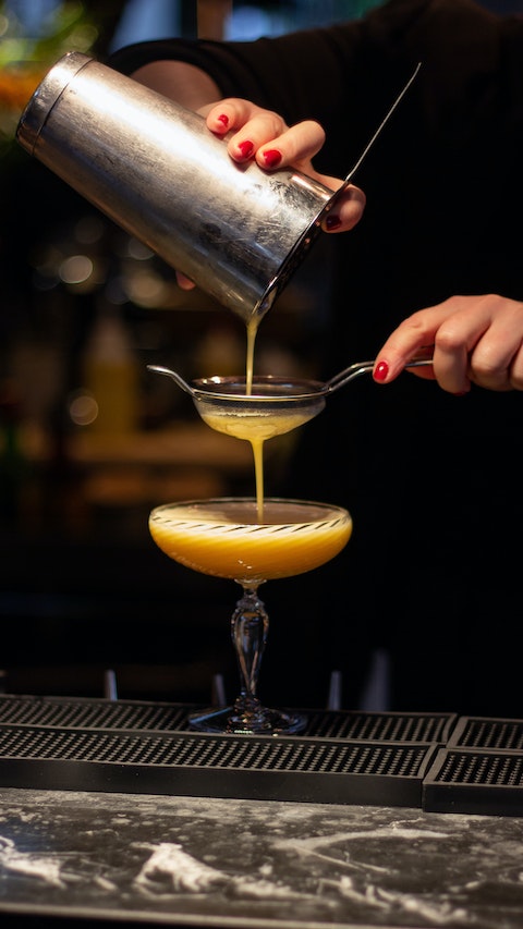 Close-up of bartender's hand pouring a freshly made cocktail through a strainer into a glass.